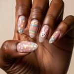 Valentines Nails Designs That Feel Chic and Modern Hand with almond-shaped Easter nail designs featuring pastel polka dots, colorful horizontal stripes, and a cute bunny face accent nail on a nude base.