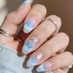 Pink Valentines Nails That Feel Chic, Glossy, and New Almond-shaped nails with a dreamy cloud design in soft blue and white, featuring a metallic heart outline and a sparkly accent nail, styled as blue valentine nails.