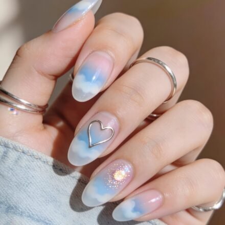 Cool-Girl Blue Valentine Nails That Look Expensive Almond-shaped nails with a dreamy cloud design in soft blue and white, featuring a metallic heart outline and a sparkly accent nail, styled as blue valentine nails.