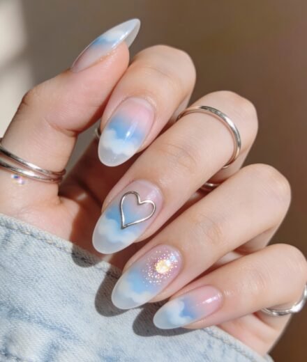 Almond-shaped nails with a dreamy cloud design in soft blue and white, featuring a metallic heart outline and a sparkly accent nail, styled as blue valentine nails.