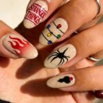 Beige almond-shaped nails with speckled detail, each featuring a unique Stranger Things design including red flames, the show's logo, multicolored Christmas lights, a black spider, and a shadowy shape with a red dot.