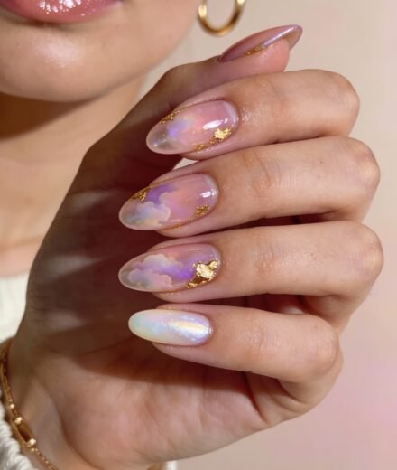 Long almond-shaped nails with a dreamy, translucent pink and gold design featuring soft pastel clouds and hints of iridescence.
