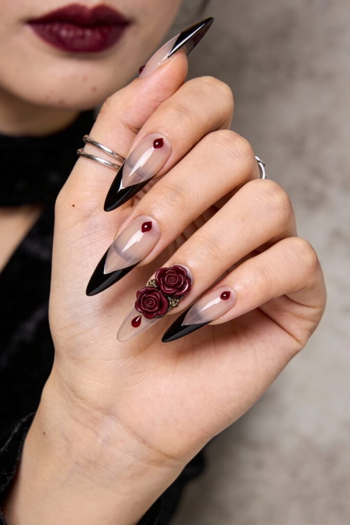 Gothic Valentines Nails That Feel Dark and Romantic 1 Hand with sharp stiletto gothic valentines nails designed with black French tips, deep red droplets, and 3D dark red roses as a romantic centerpiece.