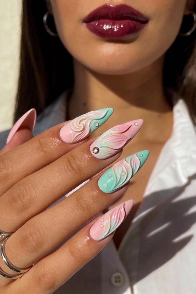 Hand with long stiletto nails painted in pink and green with sculpted 3D swirls, white pearl accents, and a glossy finish, creating a dreamy, pastel pink and green nails aesthetic.