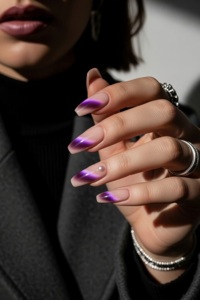 Hand with medium-length square nails in a nude base and purple chrome diagonal tips, finished with a single pearl accent for a sleek purple winter nails design.