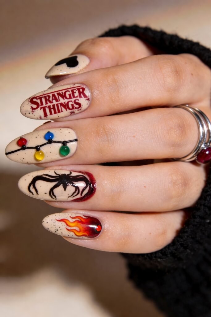 Speckled beige nails with vibrant Stranger Things nail art, including the series logo, Christmas lights, a black spider emerging from red paint, and a red-orange flame with a gem accent.