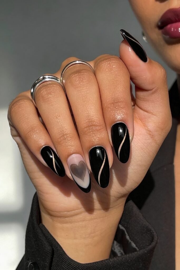 Black Valentines Day Nails That Feel Chic And Romantic 2 Hand with black valentines day nails combining glossy polish, delicate gold swirl accents, and a translucent heart on the ring finger for a romantic, modern look.