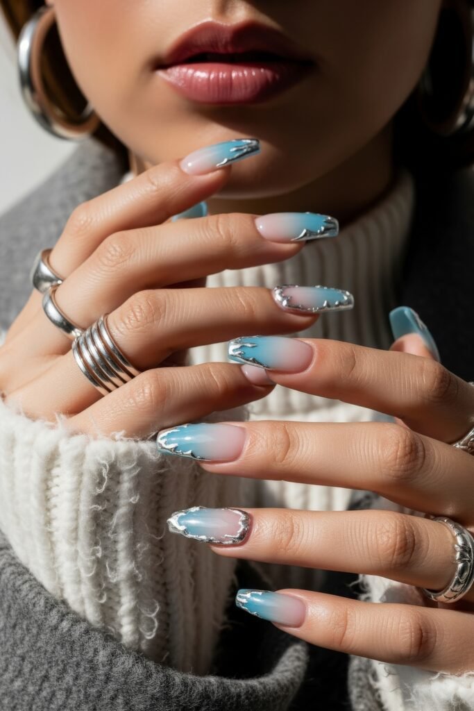 Close-up of hands with square-shaped nails showcasing a soft icy blue ombré and chrome silver borders, styled for a cozy winter aesthetic.