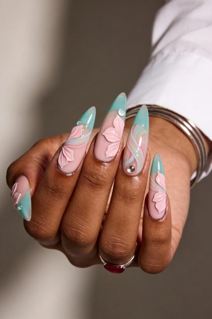 Long stiletto nails with soft pink and green ombré tips, detailed with 3D floral petals, swirled designs, and gem accents for a textured, spring-inspired pink and green nails design.