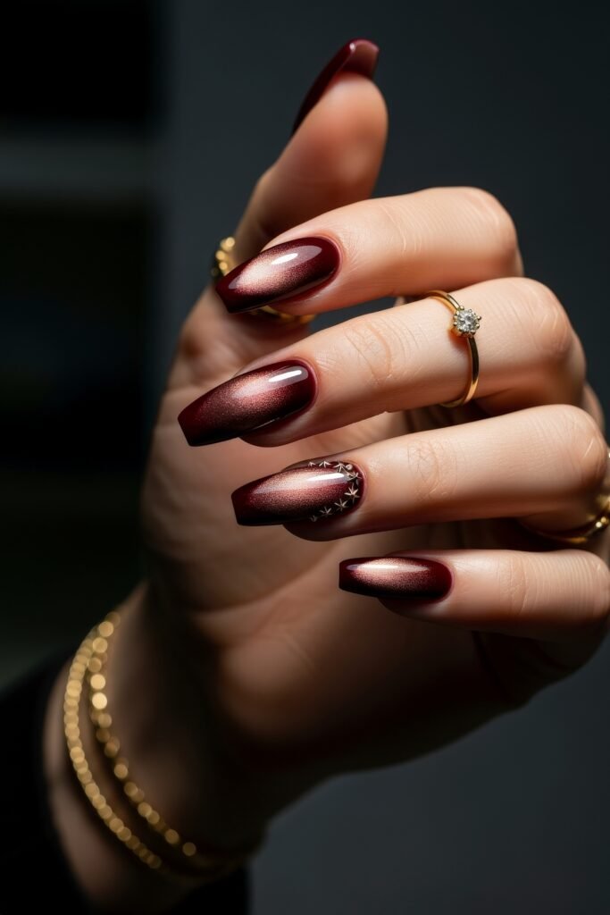 Long square nails in rich metallic burgundy with a cat-eye shimmer effect and subtle star embellishments, offering a luxurious and cozy winter look.