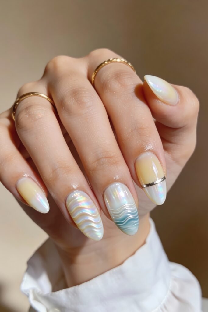 3d Nail Art Ideas That Look Luxe and Wearable 19 Pearlescent almond nails in pastel yellow and white gradients, decorated with 3d wave textures and chrome detailing, including soft blue accents and a metallic ring embellishment.