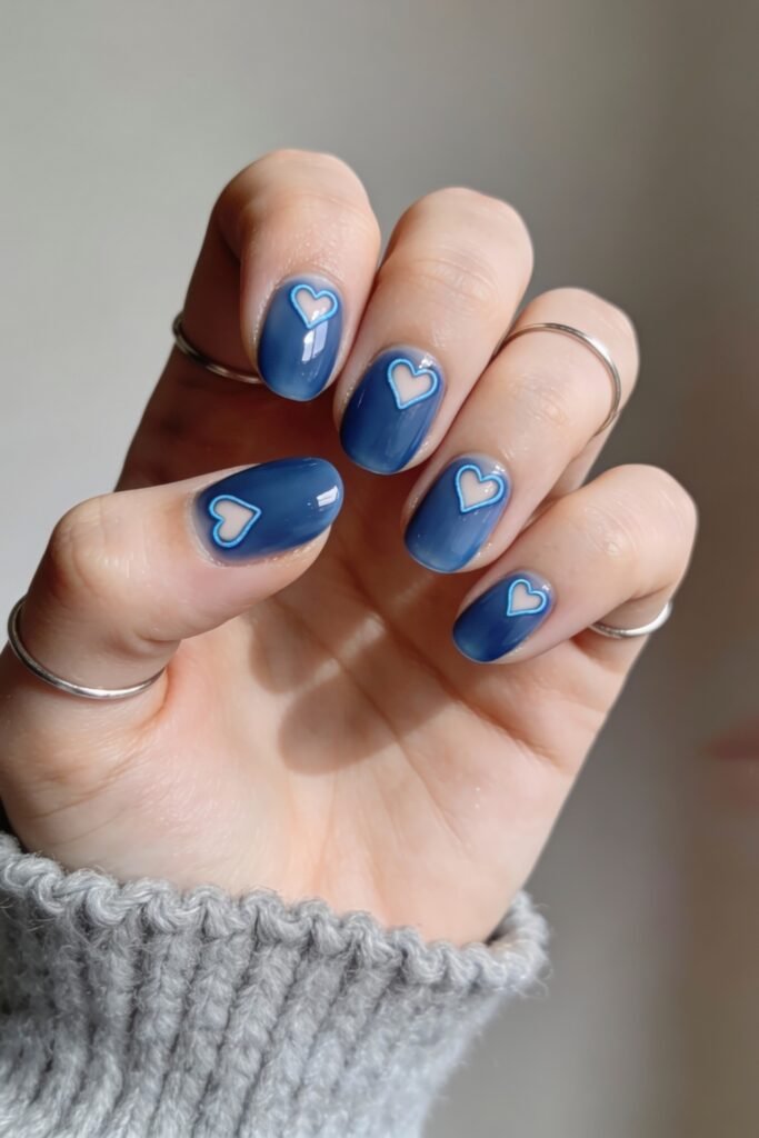 Short round nails in a vibrant blue shade with white and blue outlined hearts on each nail, creating a bold and charming blue valentine nails effect.