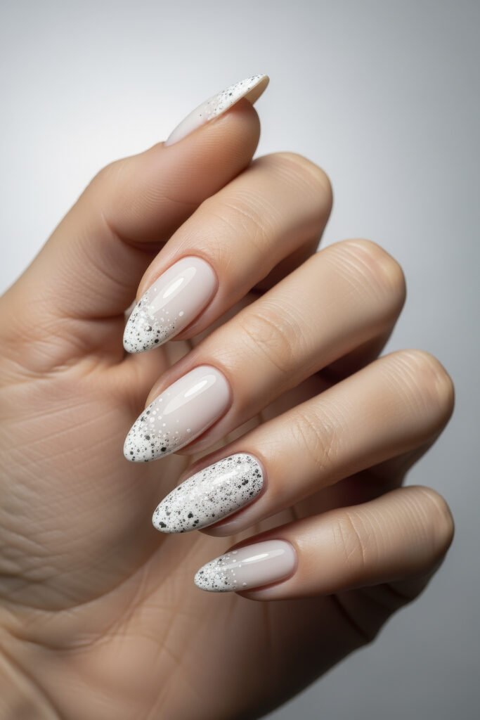 Milky White With Chrome Nails That Look Luxe 20 Almond-shaped nails with a sheer base fading into white glitter tips, featuring a mix of scattered black and silver speckles for a soft snowy effect.