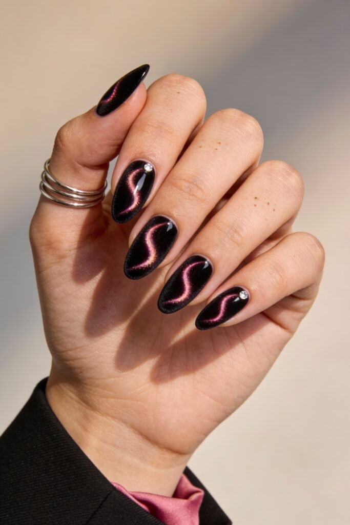 Black And Pink Nails That Look Instantly Chic 19 Glossy black almond nails with a pink cat-eye shimmer running through each nail, subtly adorned with tiny silver studs, offering a sleek black and pink nails look.