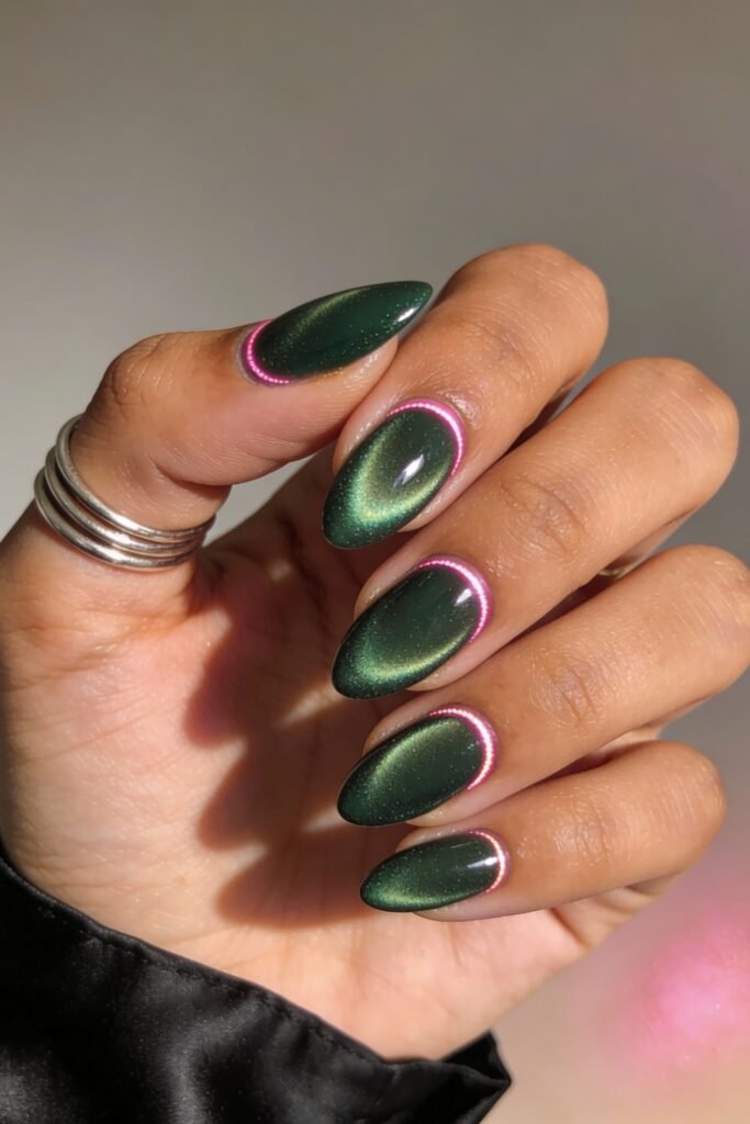 Oval nails painted in a deep shimmering green with a subtle cat-eye effect, accented by a thin neon pink outline near the cuticle, offering a bold twist on pink and green nails.