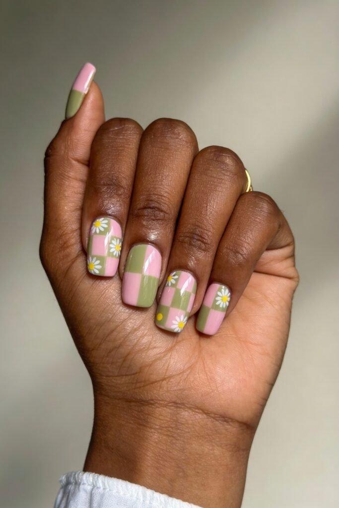 Square nails featuring a pink and green checkered pattern with white daisies and yellow dots, blending retro charm and floral whimsy in a creative pink and green nails style.