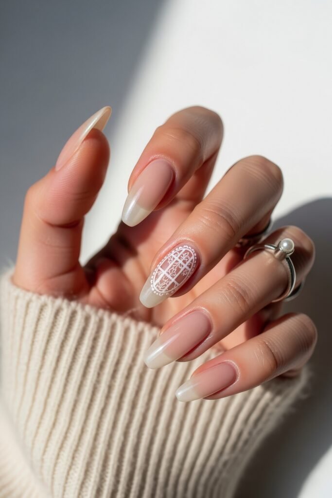 Natural-looking long nails with a soft ombré nude base and a single accent nail adorned with intricate white lace-style artwork, offering a delicate Winter Nails look.