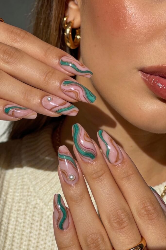 Long coffin nails with a marbled swirl pattern in pink, green, and gold, finished with a glossy top coat and pearl accents, giving a luxurious take on pink and green nails.