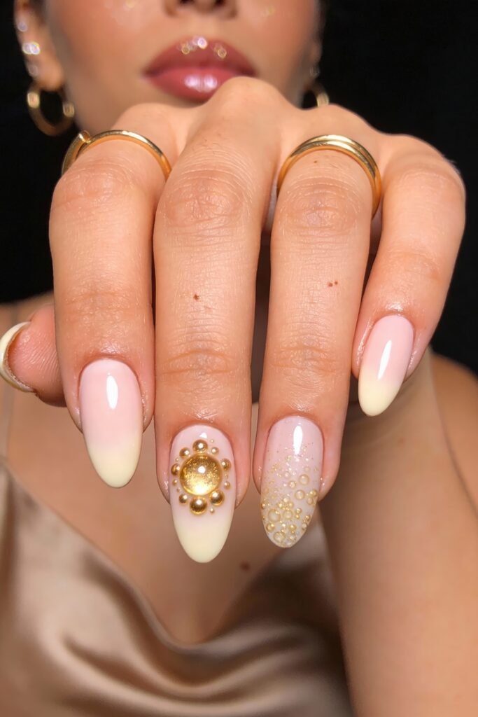 Soft ombré pink and white nails with a sun-like gold embellishment and scattered gold dot clusters on accent nails for a radiant finish.
