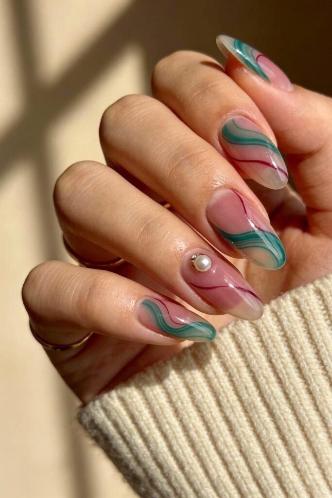 Almond nails with translucent pink bases and abstract swirl accents in green, pink, and red, finished with a pearl gem on one nail, giving a flowing and modern pink and green nails style.