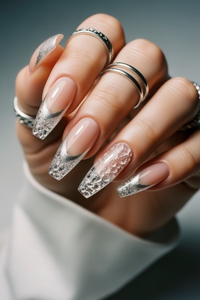 Long coffin nails with a nude base and silver glitter French tips, one accent nail featuring a 3D ice-textured design, making it a standout Winter Nails choice.