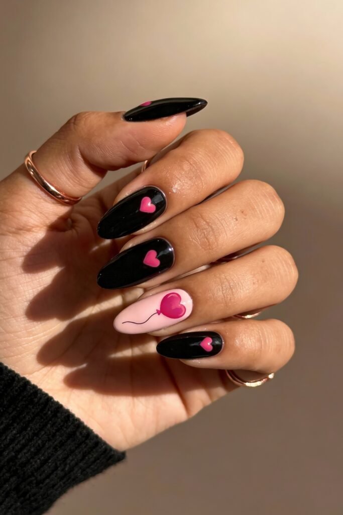 Black And Pink Nails That Look Instantly Chic 3 Black almond nails with pink heart accents on most fingers, paired with a single white nail featuring a pink heart balloon, offering a cute and minimal black and pink nails theme.