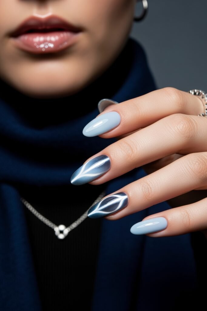 Manicured hand with a mix of glossy pale blue and navy nails, featuring shimmering leaf-like patterns that reflect a cool, icy blue winter nails theme.
