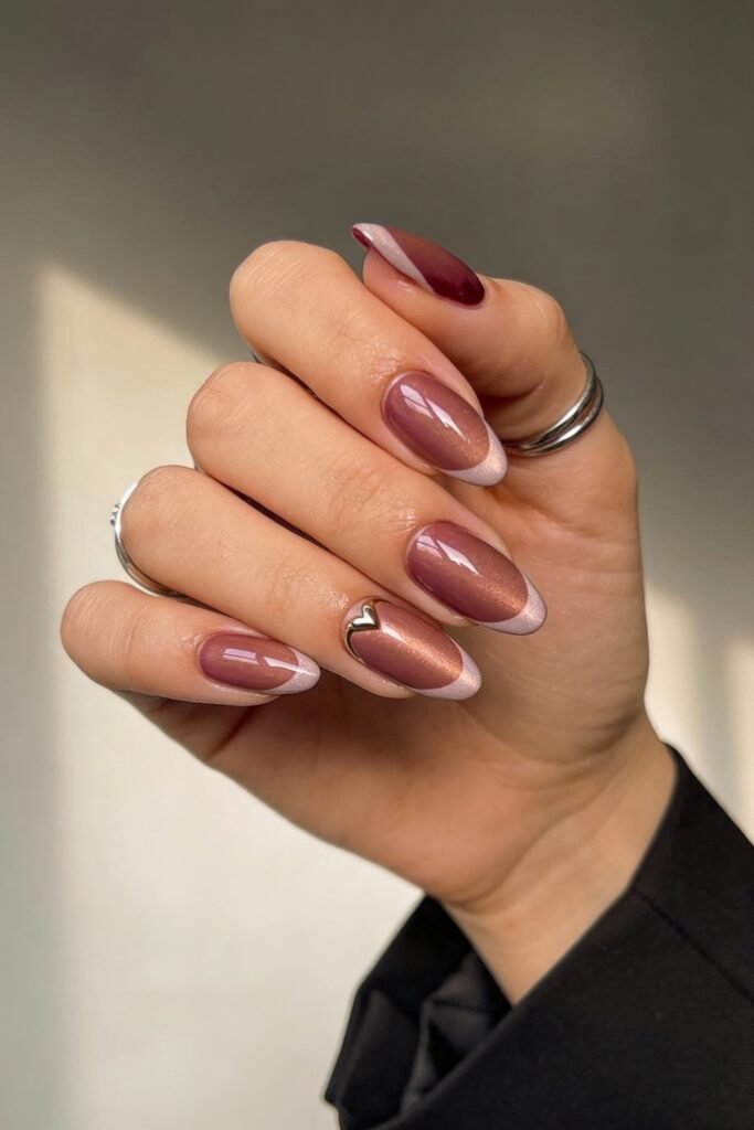 Pink Valentines Nails That Feel Chic, Glossy, and New 4 Almond-shaped pink valentines nails with a rose-gold shimmer, soft pink tips, and a small metallic heart detail.