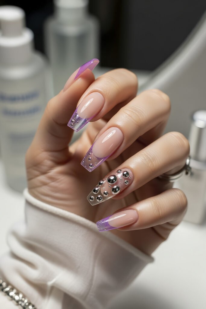Long square acrylic nails with translucent purple tips, featuring silver bubble embellishments on the accent nail, blending playful texture with glossy shine.