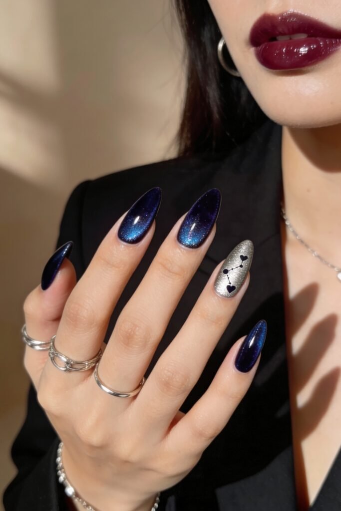 Almond-shaped nails with a galaxy-inspired design in deep navy and shimmering teal, accented by a silver glitter nail featuring a constellation of hearts, offering an edgy twist on blue valentine nails.
