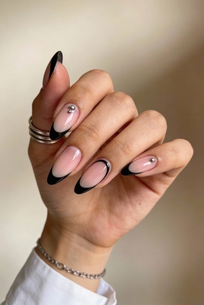 Black And Pink Nails That Look Instantly Chic 5 A variation of the previous style with almond-shaped nude nails outlined in black and tipped with solid black French tips, complemented by silver gem accents for a polished, contemporary look.