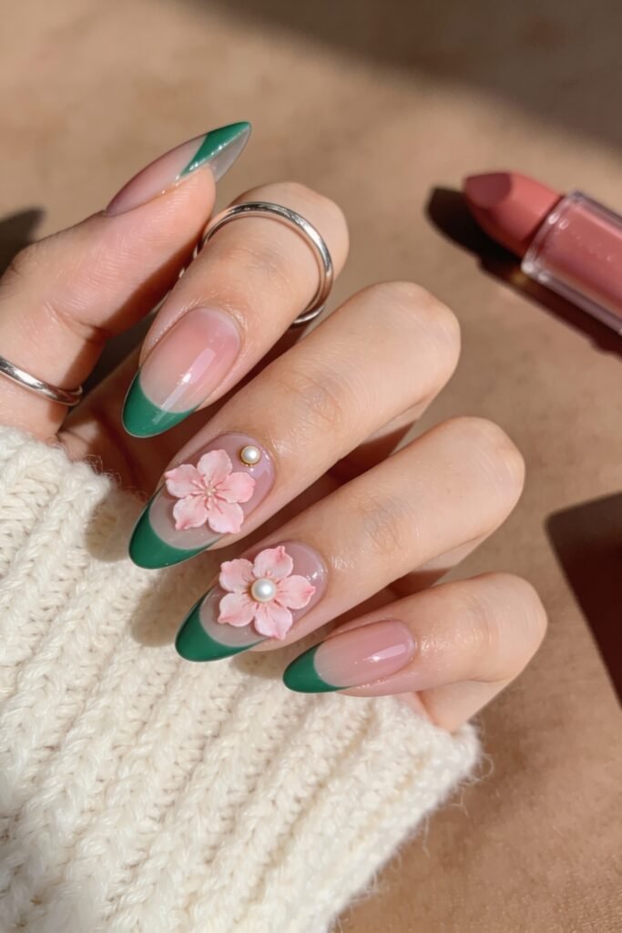 A hand featuring deep green French tips and pink 3D floral nail art, with pearl accents on two nails, blending playful and elegant tones in a pink and green nails theme.