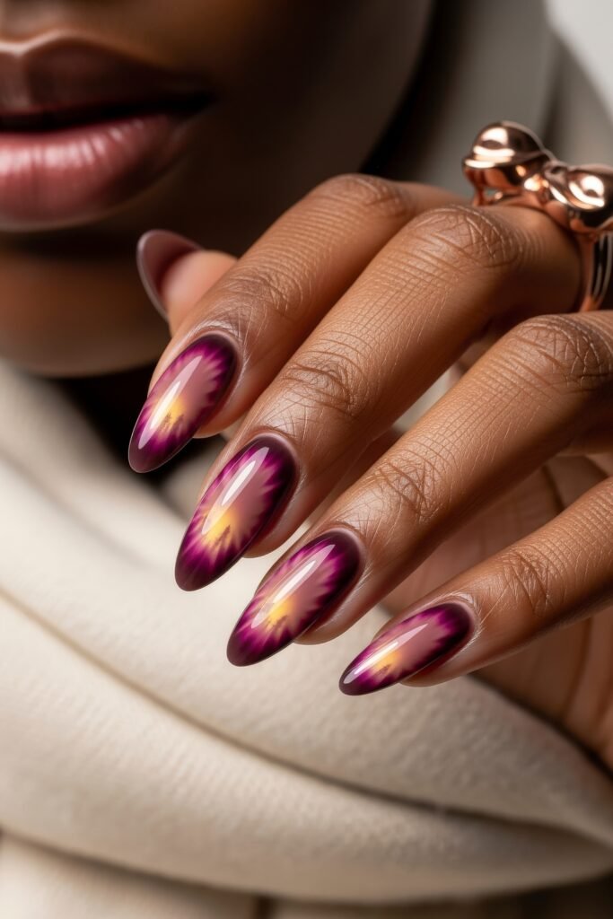 Hand with almond-shaped nails featuring a fiery blend of purple, pink, and golden hues in a radial burst design, adding a vivid twist to winter nails.