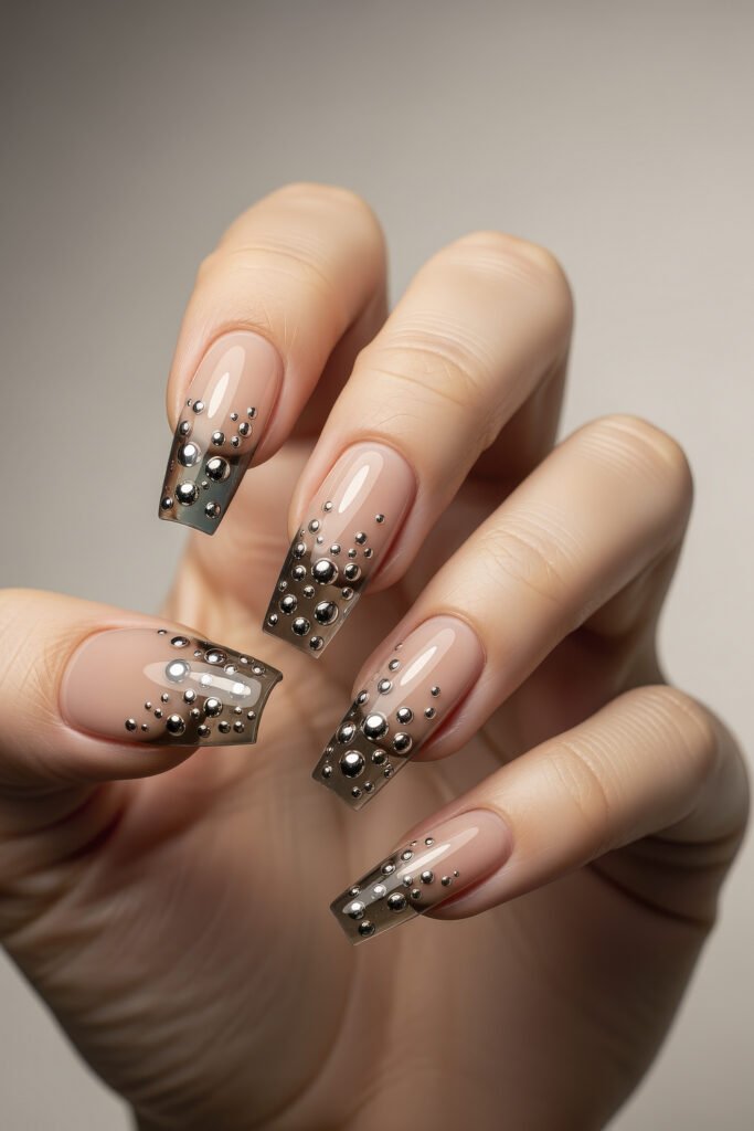 Square acrylic nails with glossy nude bases and smoky black glitter tips, decorated with clustered chrome beads for a striking 3D look.