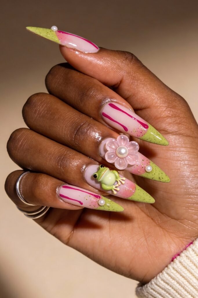 Stiletto nails with lime green and pink tips, playful red drips, and unique 3D art including a frog, flower, and pearls, offering a whimsical take on pink and green nails.