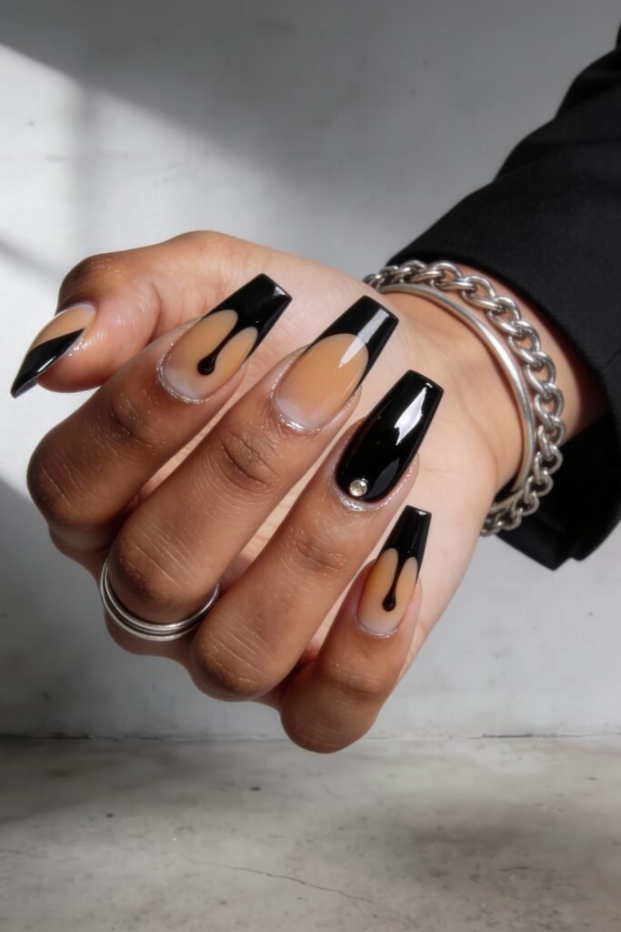 Coffin-shaped nails painted in a dramatic black and nude combo, with glossy finishes, drip effects, and a single gem detail, embodying bold street style nails.