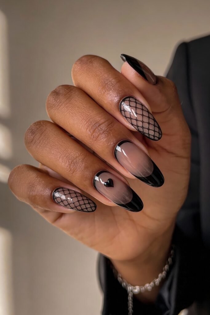 Gothic Valentines Nails That Feel Dark and Romantic 7 Hand with glossy gothic valentines nails featuring black French tips, mesh netting designs, and a tiny 3D black heart accent on a translucent base.