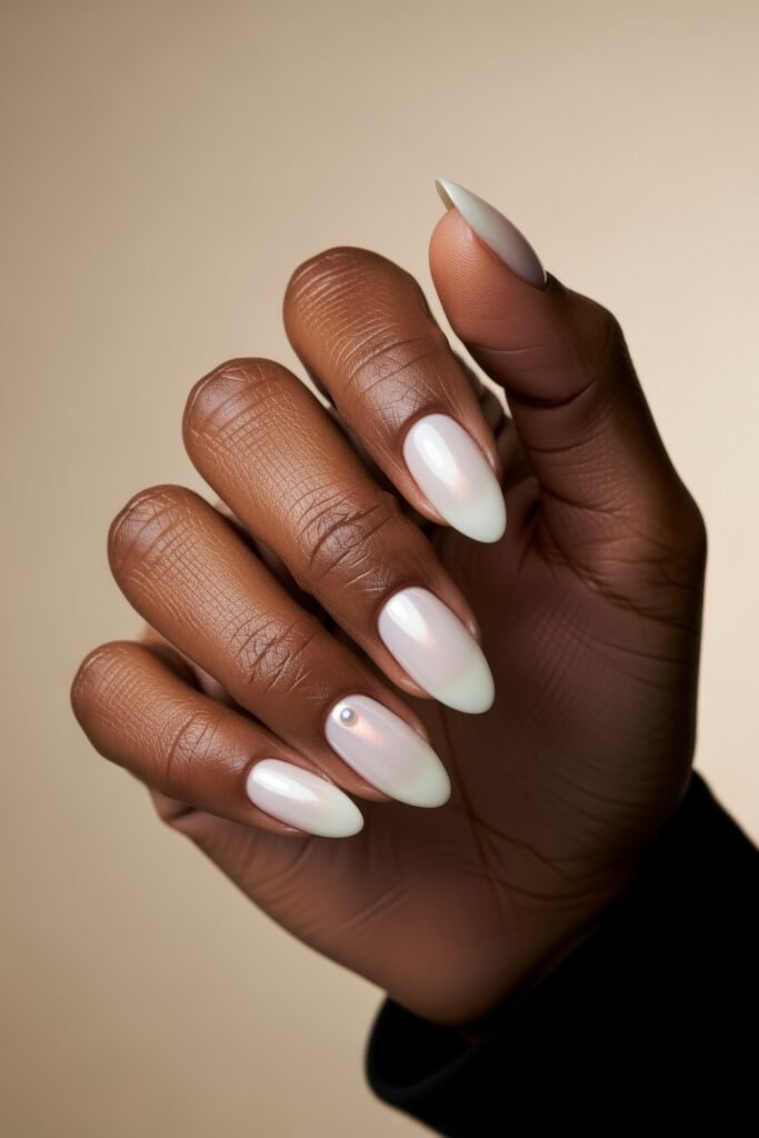 Almond-shaped nails in soft pearl white with a light iridescent finish and a delicate gem accent, offering a clean and refined Winter Nails touch.