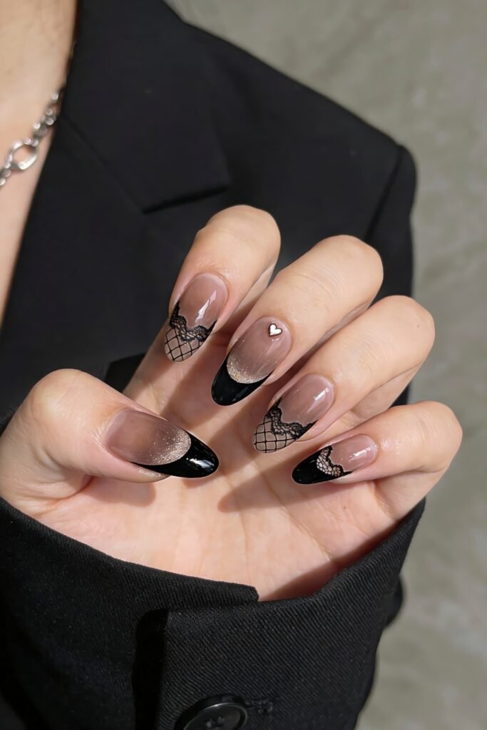 Gothic Valentines Nails That Feel Dark and Romantic 8 Sophisticated gothic valentines nails combining sheer nude polish, black French tips, lace and mesh patterns, and a small metallic heart charm.