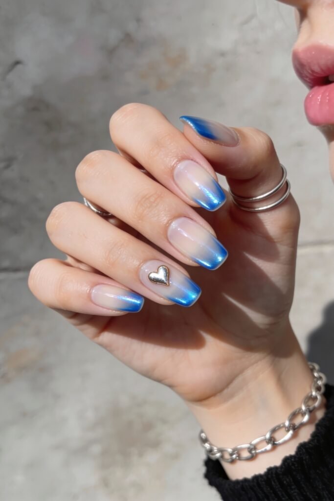 Glossy square nails with a translucent base and metallic blue ombré tips, accented with a gold heart charm on the ring finger for a sleek blue valentine nails finish.