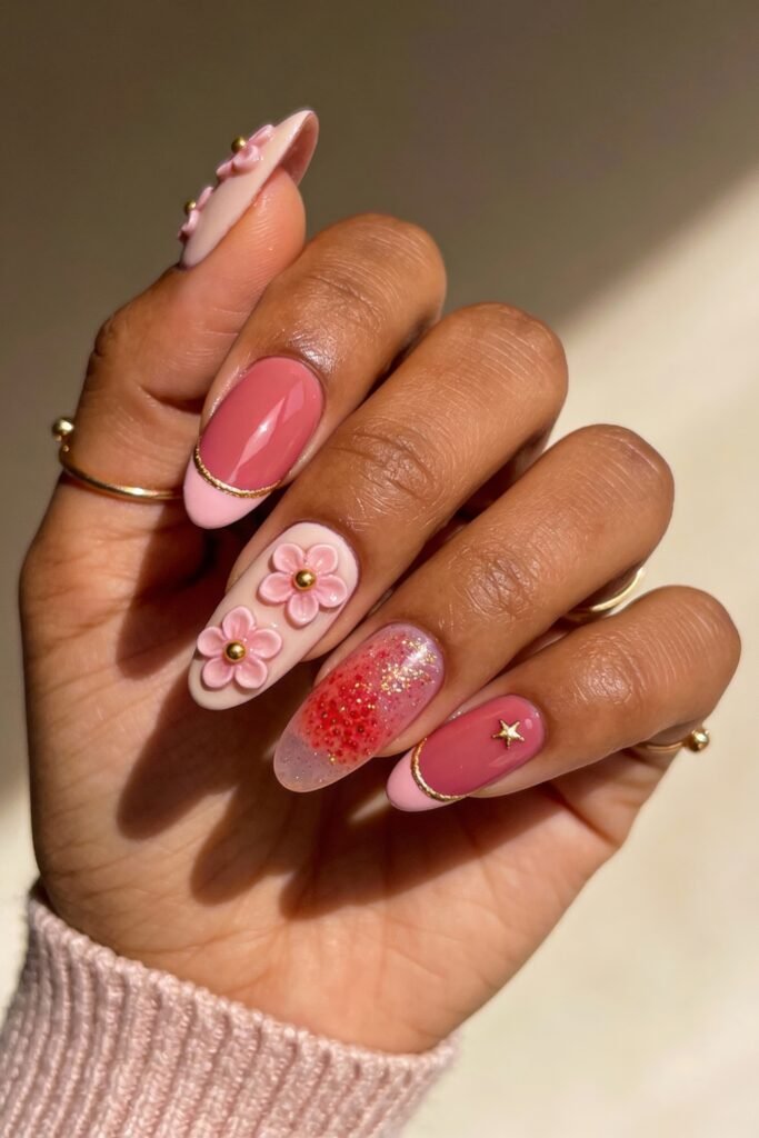 Pink and gold nails with a mix of glossy pink tips, 3D floral accents, glitter gradients, and a delicate gold star charm.