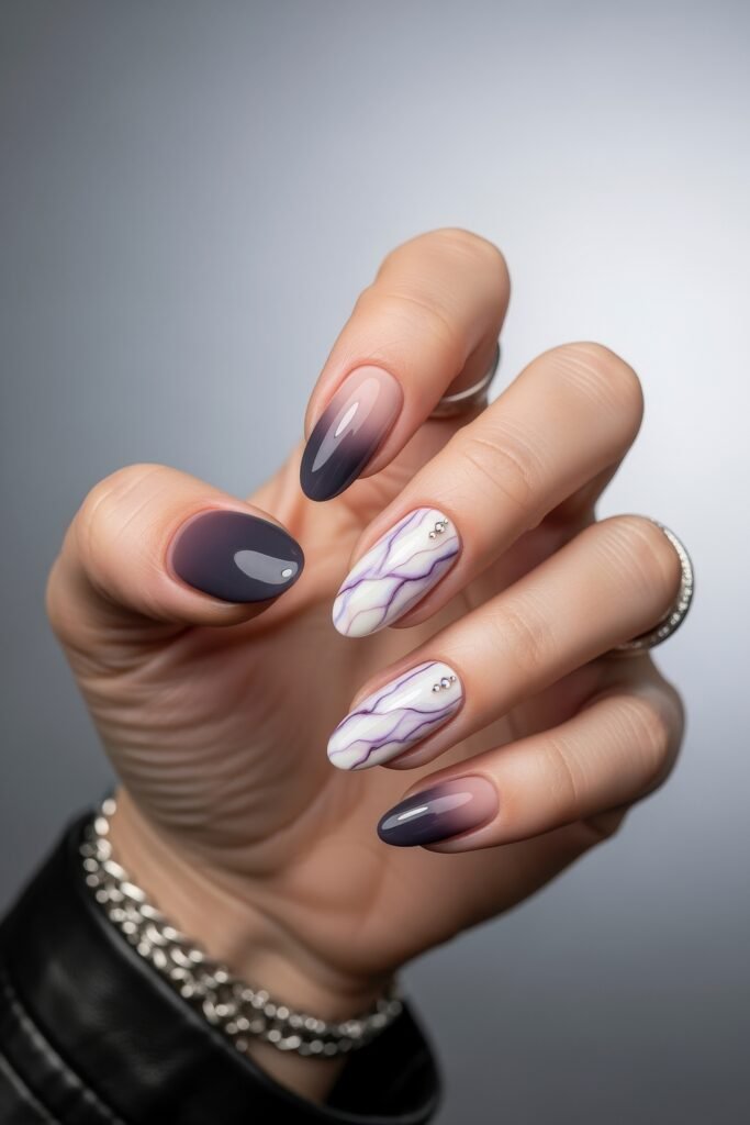 Almond-shaped nails featuring a mix of glossy plum, purple marble designs, and nude-to-dark gradient accents, finished with tiny rhinestones for a modern purple winter nails aesthetic.