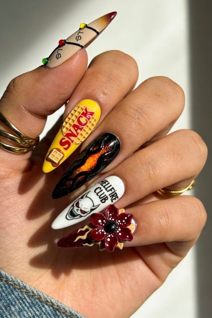 A vibrant Stranger Things nail set featuring a waffle with “SNACK” text, glowing flames, Hellfire Club skull art, and a 3D Demogorgon flower on a burgundy tip.