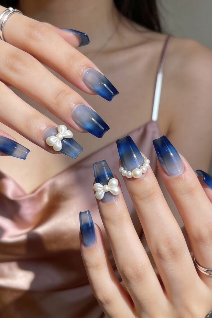 Long coffin-shaped nails with a glossy blue ombré fade, elevated by 3D pearl bows and accents, combining luxury and cuteness for a standout blue valentine nails style.