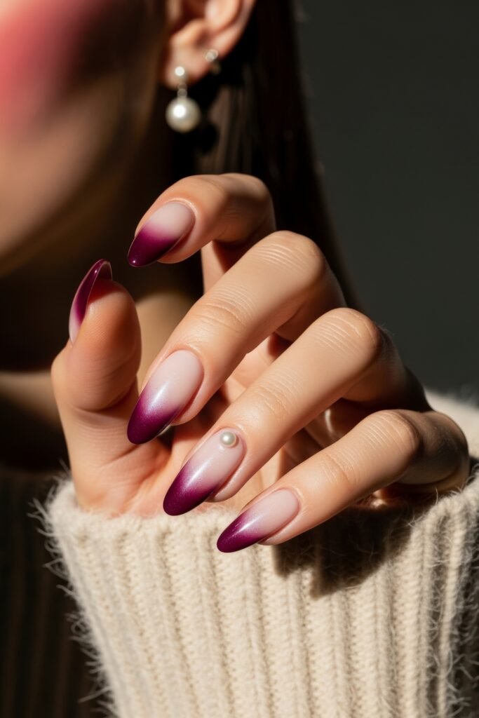 Elegant almond nails with a soft nude-to-deep plum gradient, enhanced by a single pearl embellishment, capturing a classic and cozy winter nails vibe.