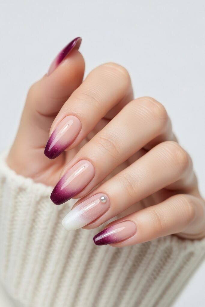 Medium almond nails in a gradient of nude to plum with a shimmer finish, including one accent nail in pearlescent white and a pearl detail, evoking a delicate winter nails design.