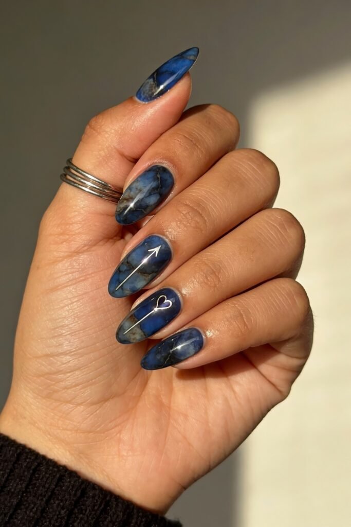 Glossy marbled blue nails with delicate silver arrow and heart line art, creating a moody and modern twist on the blue valentine nails aesthetic.