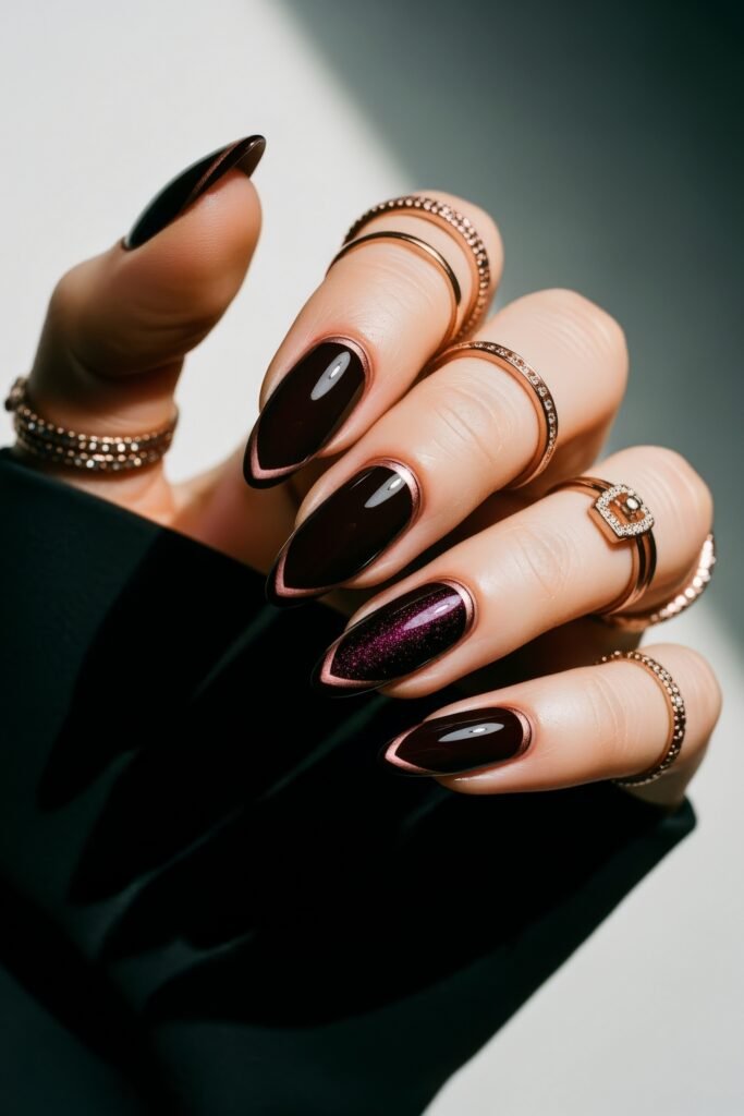 Almond-shaped nails in deep burgundy with a chrome rose gold outline, featuring one glittery accent nail for a glamorous, moody Winter Nails style.