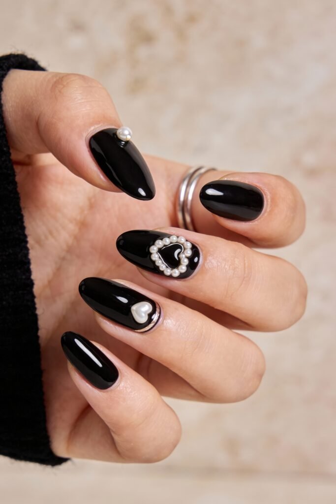 Black Valentines Day Nails That Feel Chic And Romantic 16 Oval-shaped black valentines day nails featuring glossy polish, a mini pearl stud on the thumb, and delicate pearl heart frames for a refined, romantic effect.