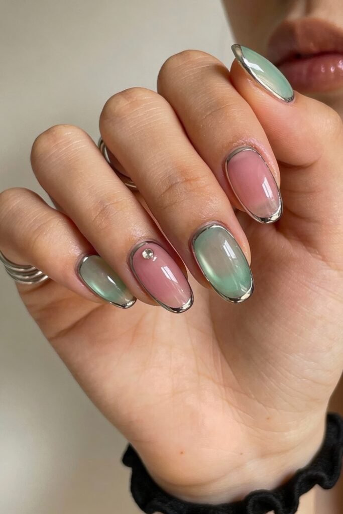 Oval nails with a translucent pink and green base framed in silver chrome, accented with a tiny gem on one nail for a minimal yet chic pink and green nails style.